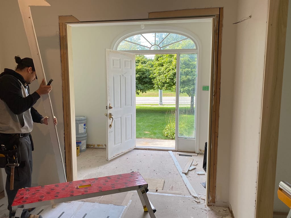 Finish carpenter removing raised and uneven drywall beside a door jamb to prepare a flat area for casing installation.