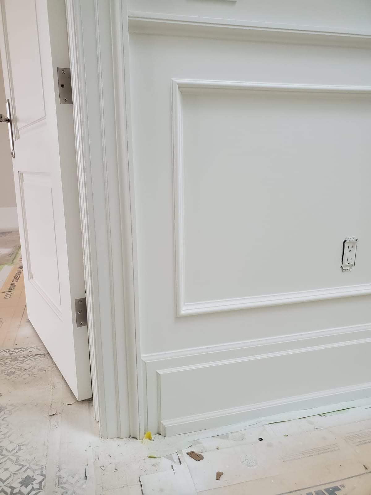Close-up of white baseboard, shoe moulding, door casing and wall paneling meeting beside an interior doorway