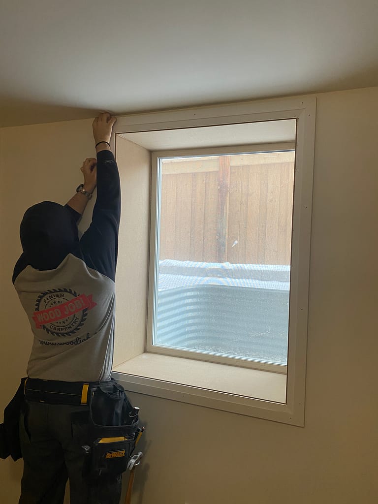 Carpenter installing window casing in Milton basement.