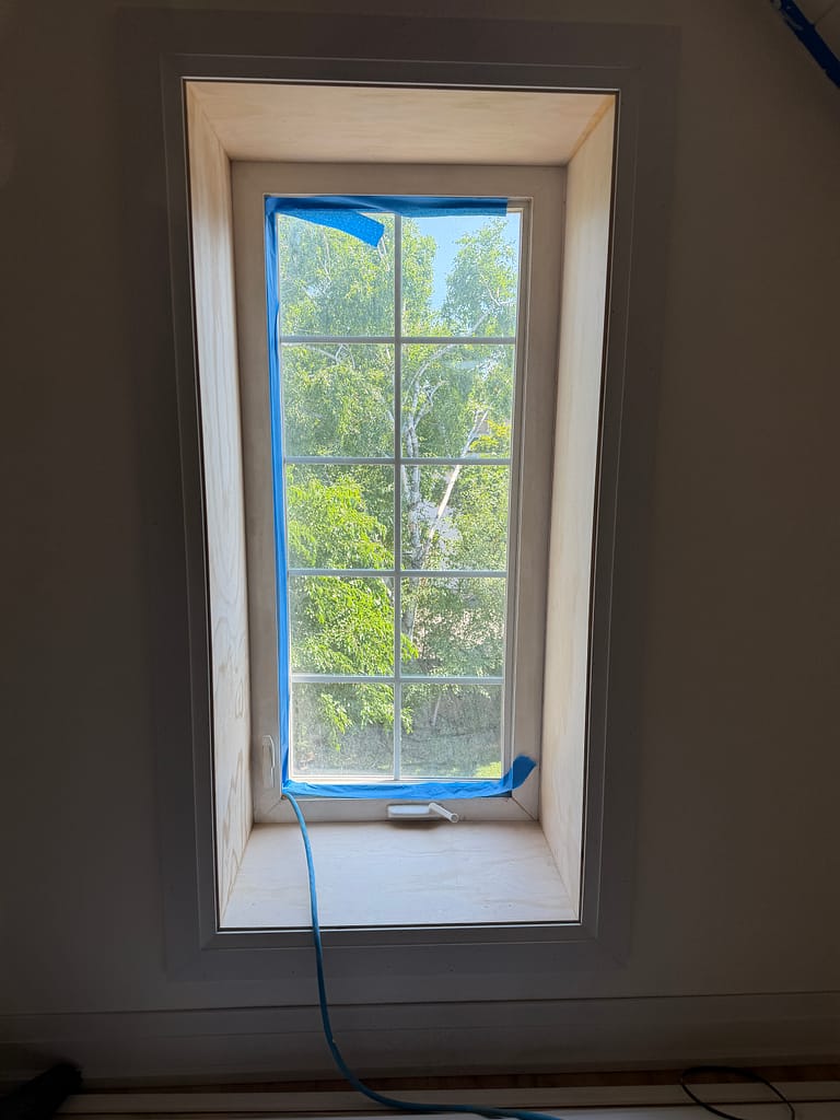 Tall attic window fitted with deep plywood jamb extensions and white casing