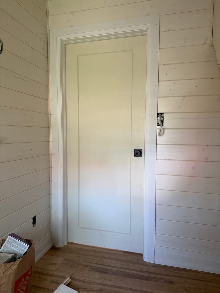 One-panel bathroom door installed with white casing against shiplap walls