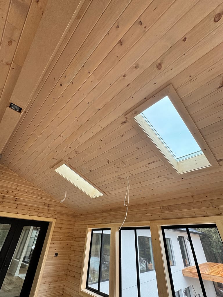 Two skylights framed within a natural wood shiplap ceiling in an Oakville cabin addition