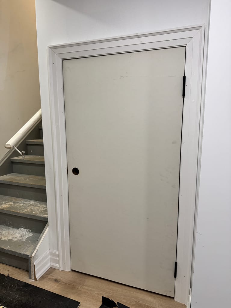 Large custom basement storage door built under stairs with wide casing and baseboard trim.