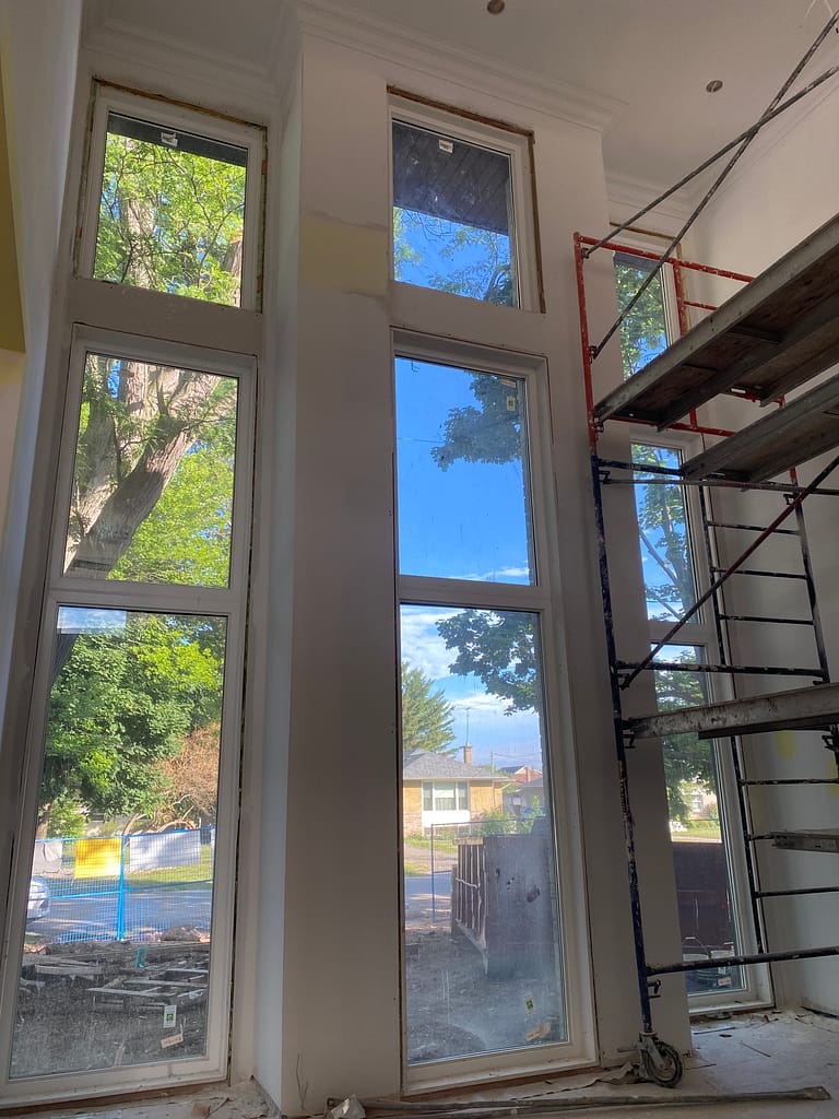 Tall window openings prepared for trim and jamb extensions with scaffolding in an Oakville home.