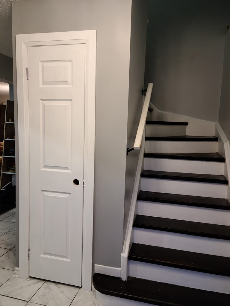 White panel closet door with casing and a painted grey wall beside a staircase in a Milton entryway