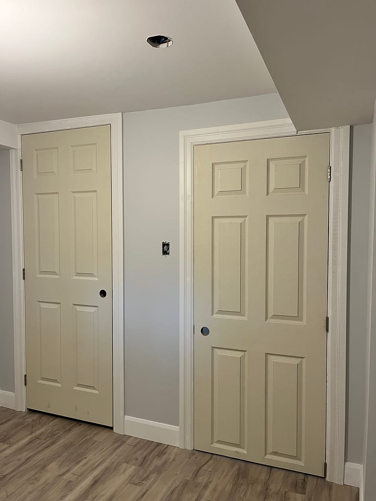 Pre-hung basement interior door cut heavily at the bottom because of a low opening, showing a narrow lower rail and bottom hinge close to the floor.
