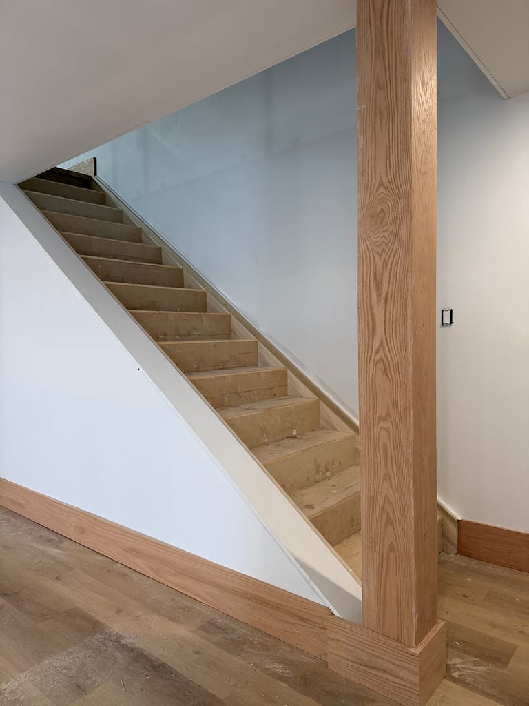 Stain-grade red oak baseboard wrapped around a custom stair post and continued along the wall