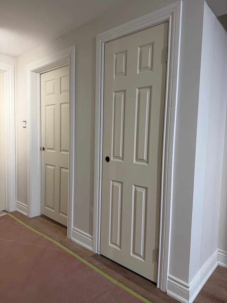 Six-panel basement doors installed with casing and baseboards in a finished basement hallway.
