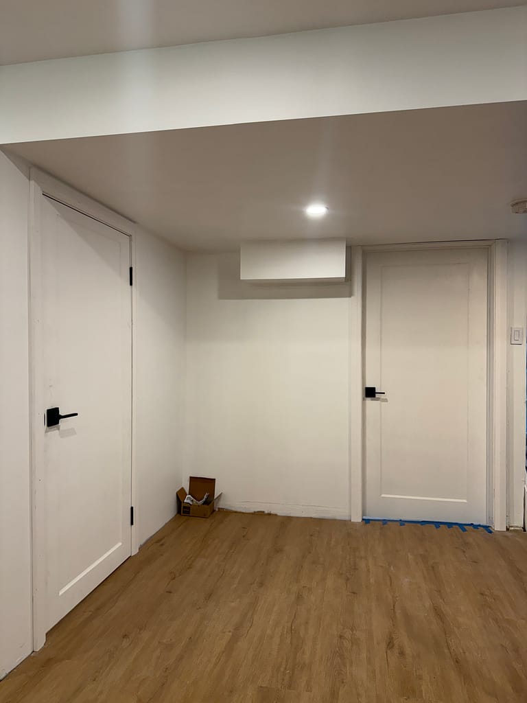 Two white basement doors installed with casing and black hardware in a Burlington home