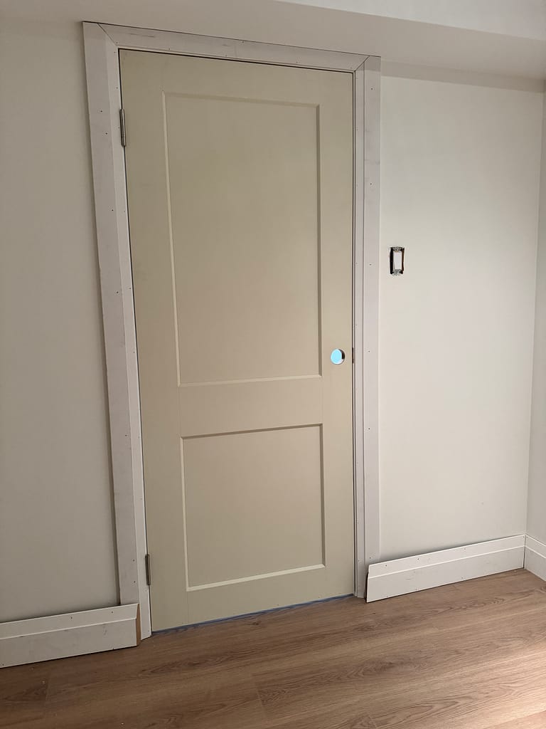 Two one-panel basement doors installed under a low ceiling with casing and baseboards.
