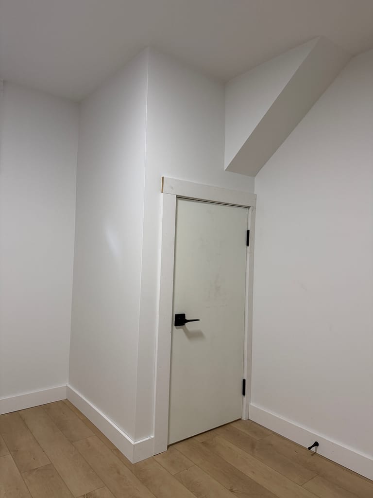 Short flush basement door fitted with Craftsman-style casing below a ceiling bulkhead