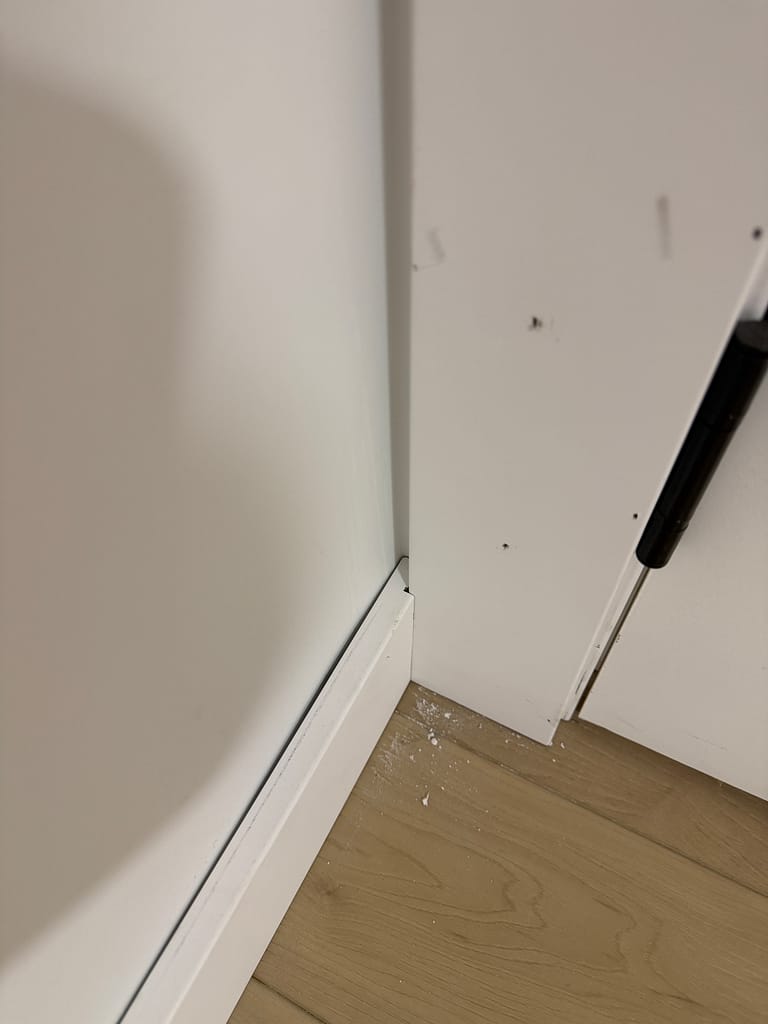 Close view of flat-stock baseboard being fitted where it meets door casing