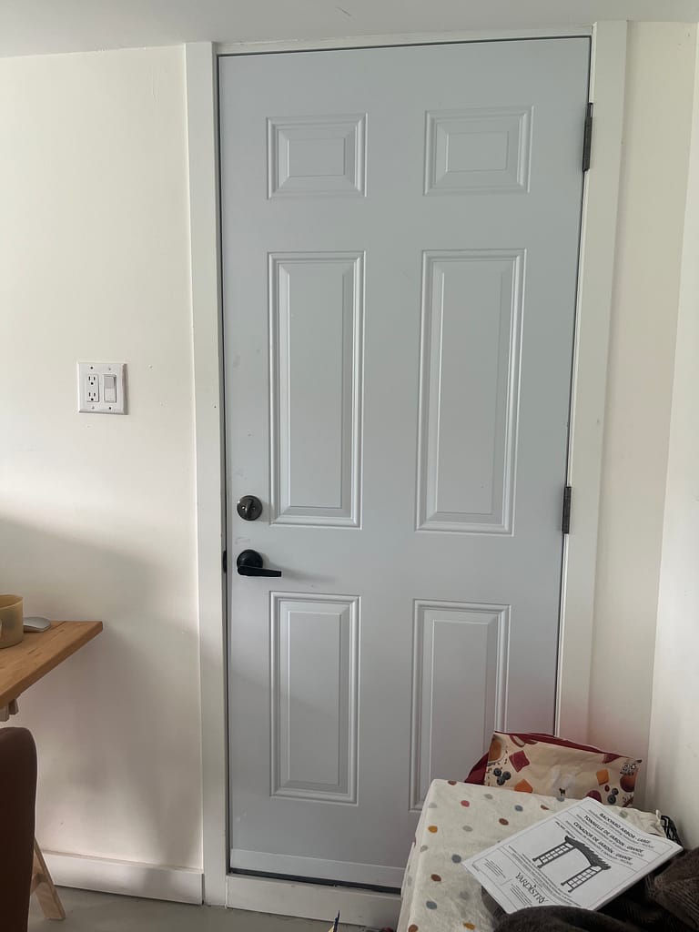 Existing six-panel metal garage entry door before replacement in a Burlington home