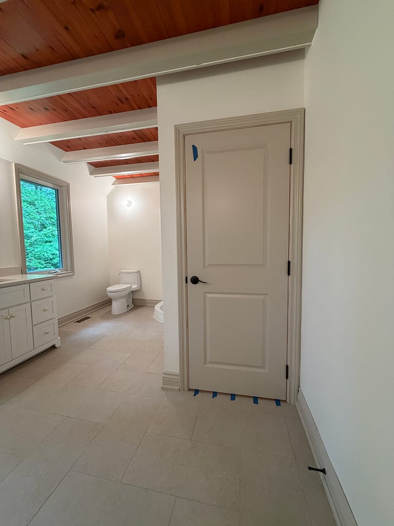 Bathroom entrance with interior door, window casing, baseboards and ceiling beam covers