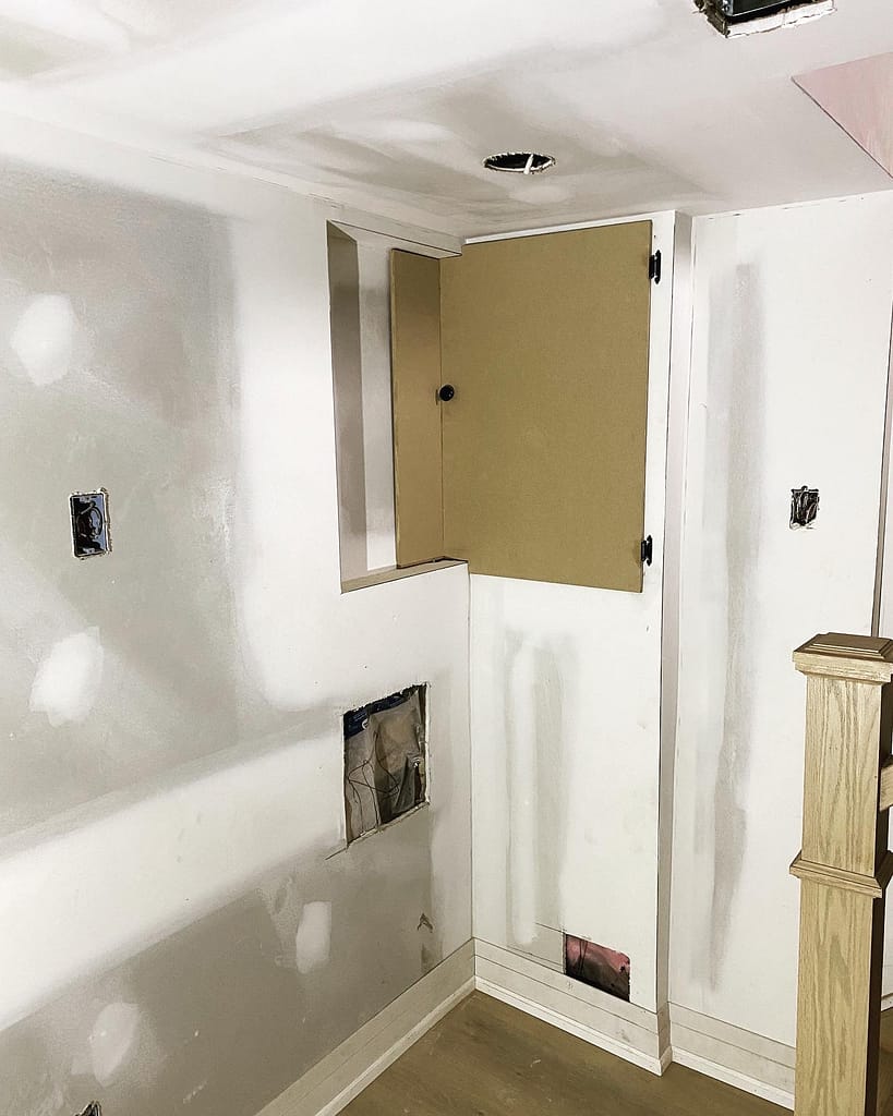 A custom-built wood wall panel enclosure hiding an old electrical fuse box seamlessly inside updated hallway trim.
