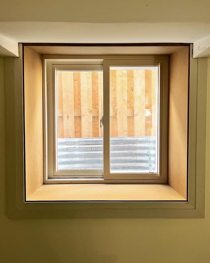 Framed basement window with wooden backdrop by finish carpenter in Oakville.