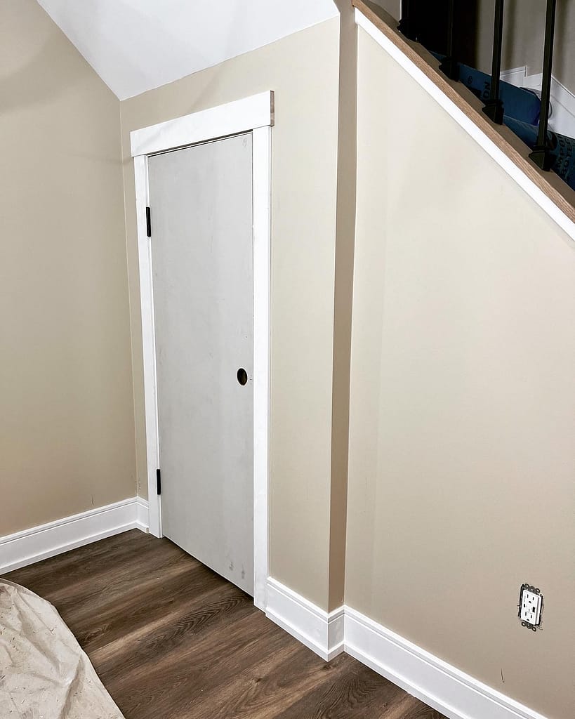 Custom basement storage door installed under stairs with casing and baseboard trim around a low opening.