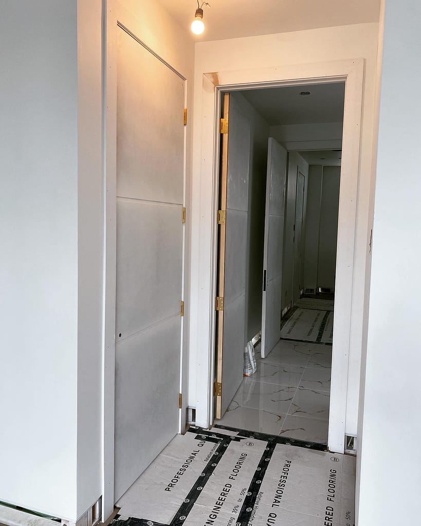 Two tall interior door openings with solid-core doors, brass hinges and custom casing during an Oakville installation.