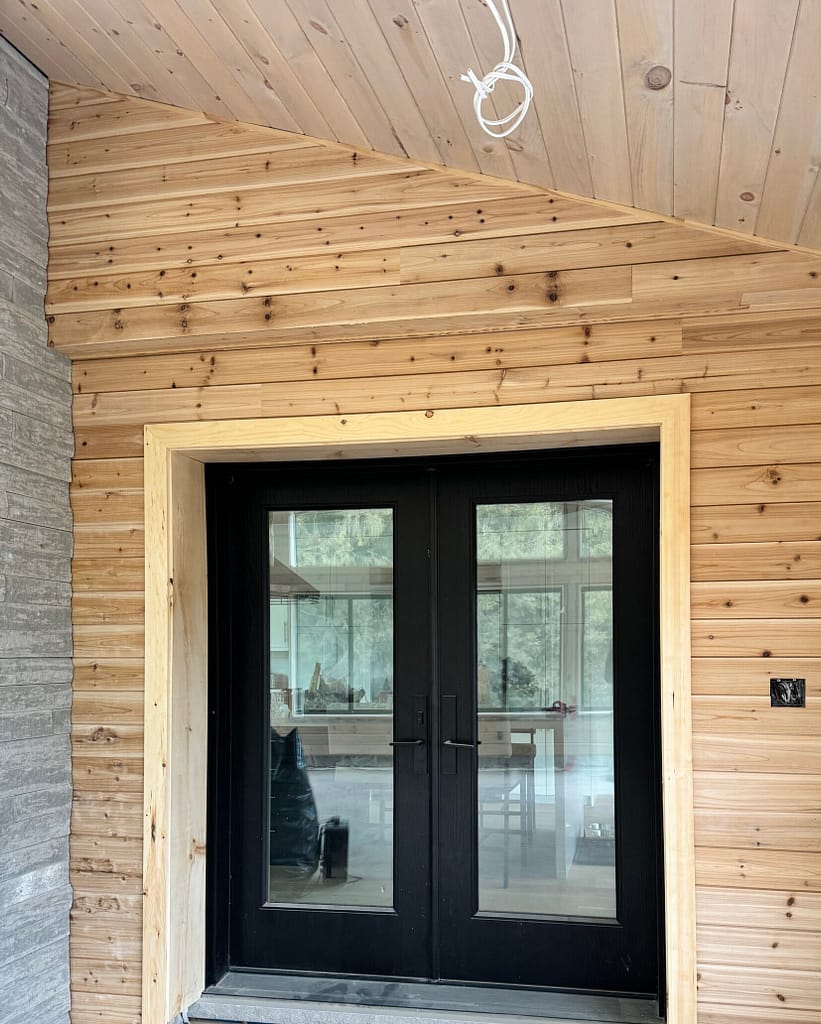 Black glass French doors framed with natural wood trim in an Oakville shiplap cabin addition