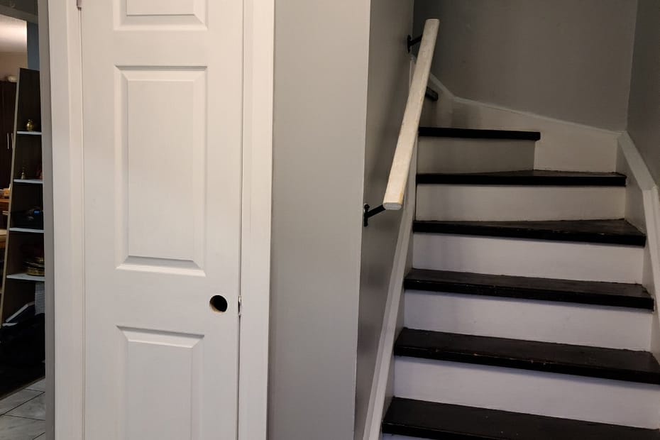 White panel closet door with casing and a painted grey wall beside a staircase in a Milton entryway